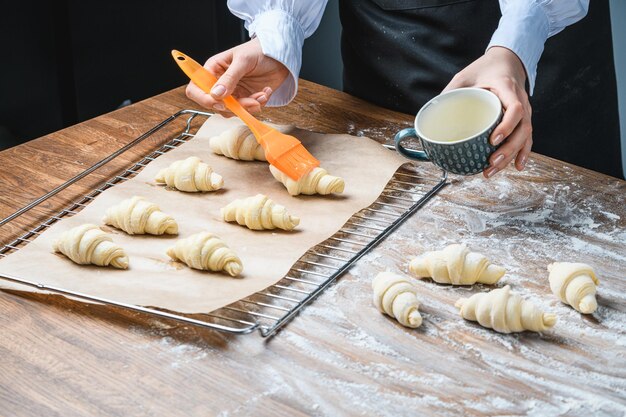 El cocinero engrasa croissants de huevo en la mesa con ingredientes.