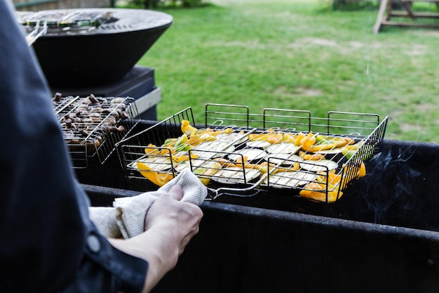 El cocinero fríe verduras a la parrilla Un hombre con una toalla sostiene una parrilla con verduras Foto horizontal