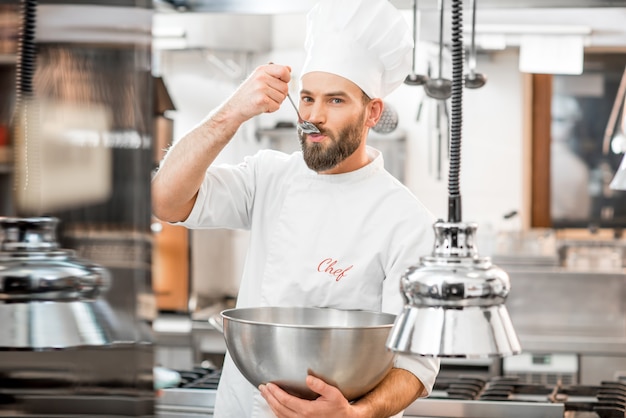 Foto cocinero guapo chef degustación con comida de cuchara en la hermosa cocina del restaurante