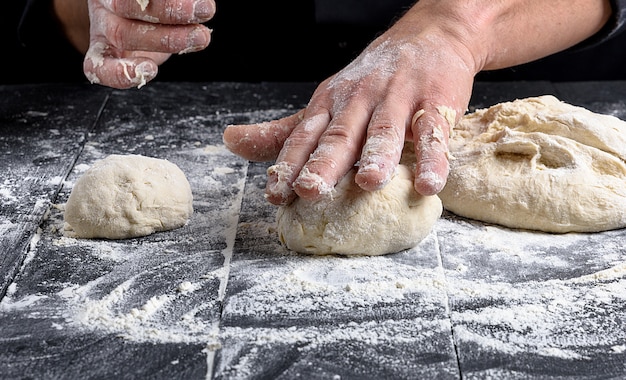 Cocinero haciendo bolas de masa en una mesa de madera negra