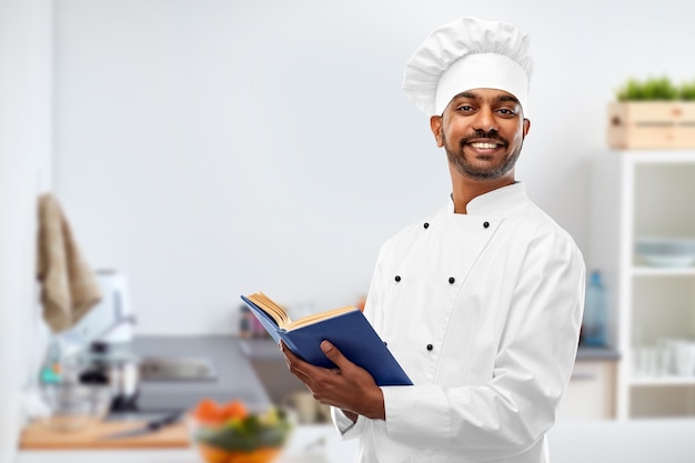 cocinero indio feliz con libro de cocina en la cocina