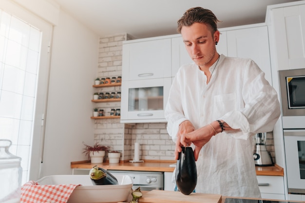 Cocinero joven caucásico en casa. Va a cortar la berenjena para empezar a cocinarla.