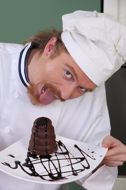 Cocinero joven divertido que come un pedazo de torta