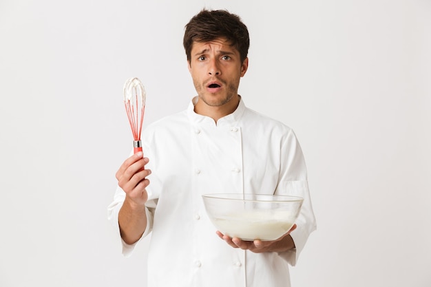 Cocinero joven sorprendido confuso aislado en la cocina blanca.