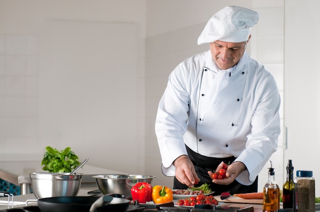Un cocinero maduro feliz y sonriente preparando una comida con varias verduras
