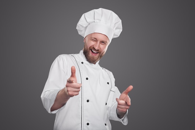 Foto cocinero masculino contenido en uniforme de chef blanco apuntando a la cámara mostrando que queremos que usted gesto por concepto de contratación