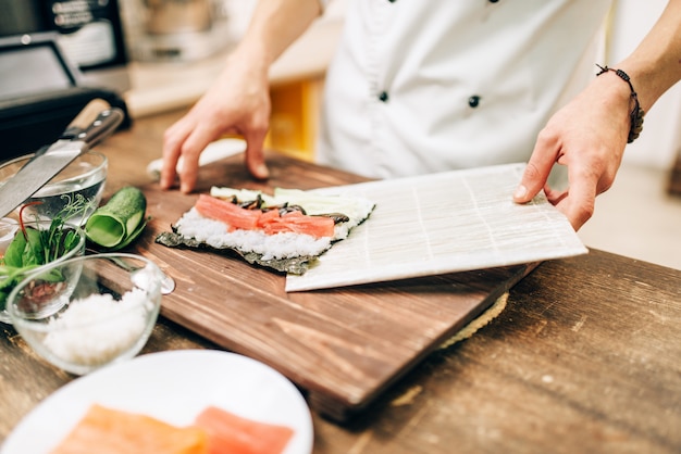 Cocinero masculino haciendo sushi en la mesa de madera, proceso de preparación de la cocina asiática.