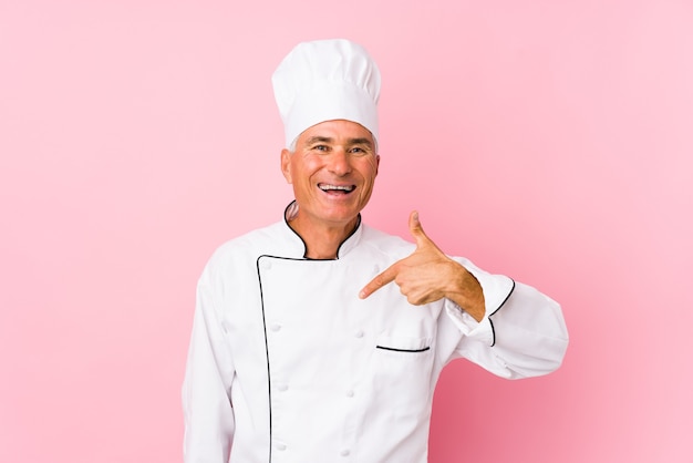 Cocinero de mediana edad hombre persona aislada apuntando con la mano a un espacio de copia de camisa, orgulloso y confiado