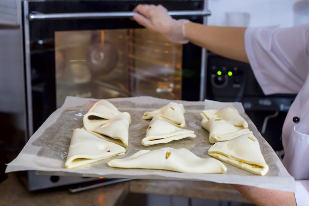 Foto el cocinero de la mujer pone soplos de queso en el molde para hornear en horno. pastas frescas en la cafetería.