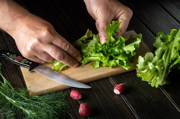 El cocinero prepara una ensalada en una tabla de cortar de cocina