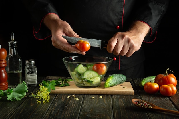 El cocinero prepara una ensalada de verduras en la cocina cortando un tomate fresco para una ensalda de vitaminas con un cuchillo