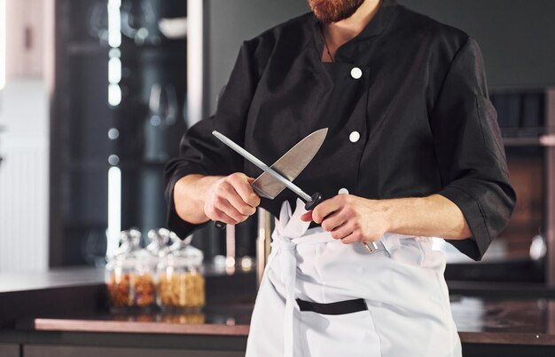 Cocinero profesional joven en uniforme de pie y preparándose para el trabajo en la cocina