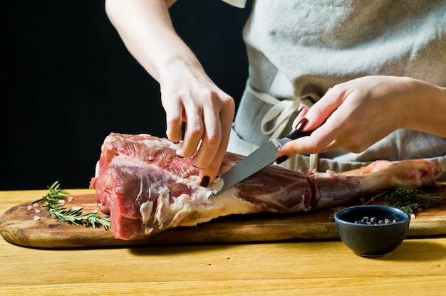 El cocinero que cocina la pierna cruda de la cabra en una tajadera de madera. Romero, tomillo, pimienta negra.