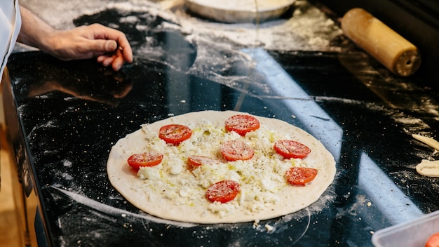 Cocinero que hace la pizza Caprese Bianca agregando aceite de oliva en la masa.