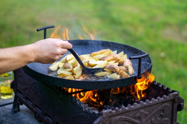 El cocinero revuelve las patatas que se fríen en un fuego abierto en aceite al aire libre