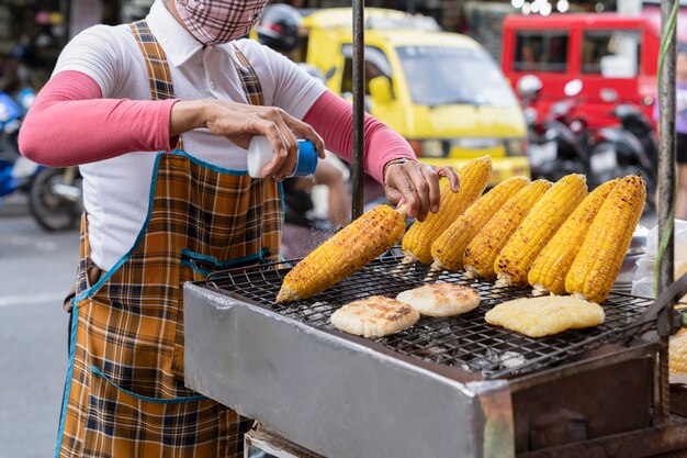 El cocinero rocía sal sobre maíz a la parrilla recién cocinado. comida callejera en Asia, Tailandia