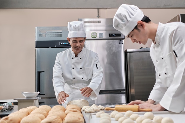 Los cocineros asiáticos en uniforme se preparan para hornear pan en una cocina inoxidable