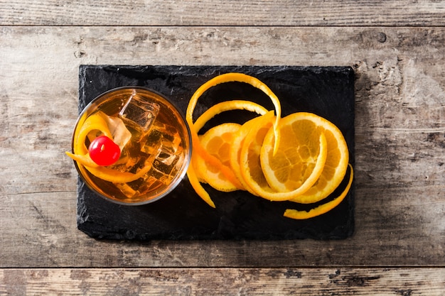 Cocktail à moda antiga com laranja e cereja na mesa de madeira