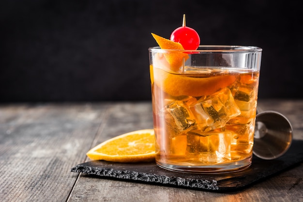 Cocktail à moda antiga com laranja e cereja no espaço da cópia de mesa de madeira