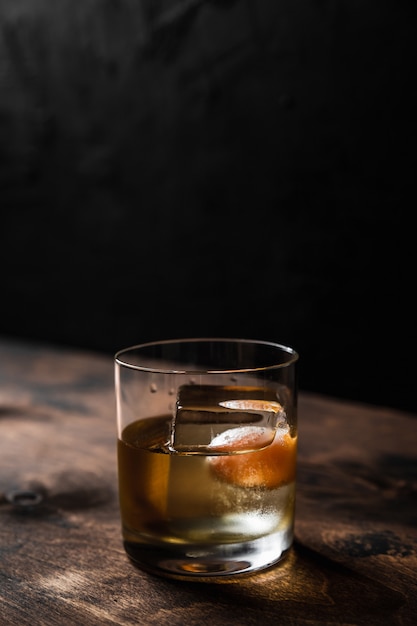 Cocktail à moda antiga em um copo de rochas com um grande cubo de gelo, luz de fundo
