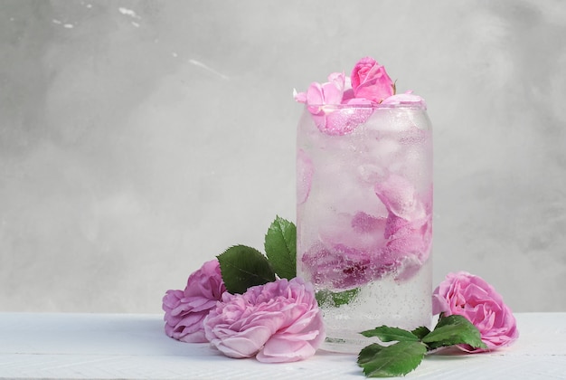 Cocktail aus hellrosa Rosenblüten-Eiswürfeln auf grauem Hintergrund mit Rosenblüten