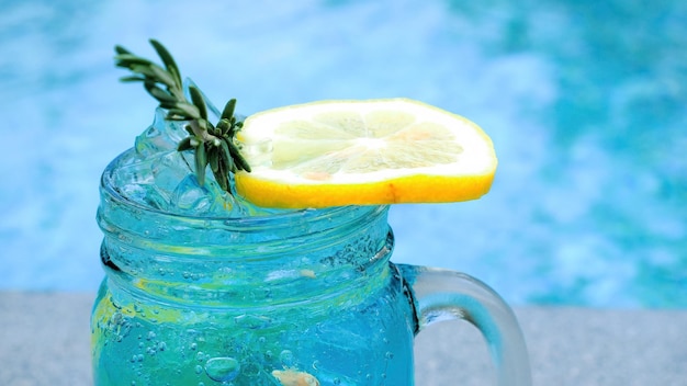 Cocktail azul gelado frio com alecrim e fatia de laranja pela piscina azul