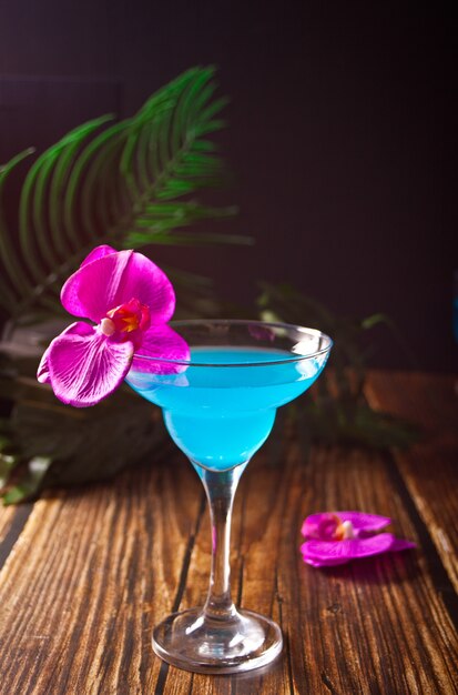 Cocktail azul tropical de verão decorado flor de orquídea roxa no fundo de madeira.