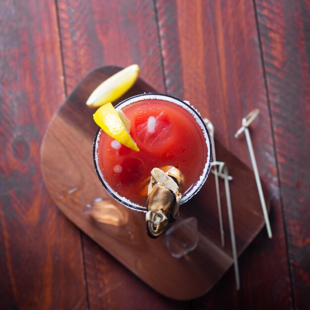 Cocktail Bloody Mary mit Eis, Salz und Snacks im Glas auf einem Holztisch. Flach liegen