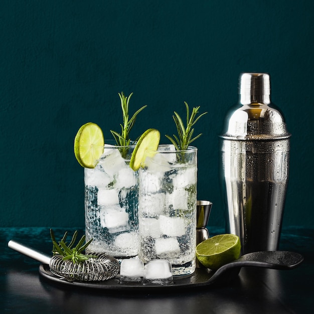 Cocktail clássico de gim e tônica com raminhos de alecrim em copos altos em uma mesa com acessórios de bar