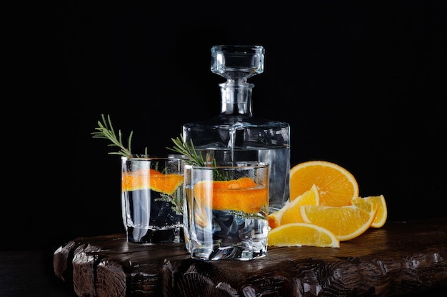 Cocktail clássico dry gin com tônica e raspas de laranja com um raminho de alecrim em uma tábua de madeira com fatias suculentas de laranja