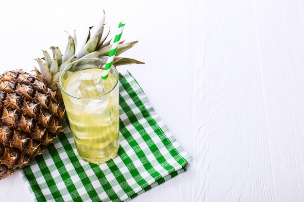 Foto cocktail de abacaxi com gelo e palha verde, sobre uma mesa branca. humor de frutas de verão.