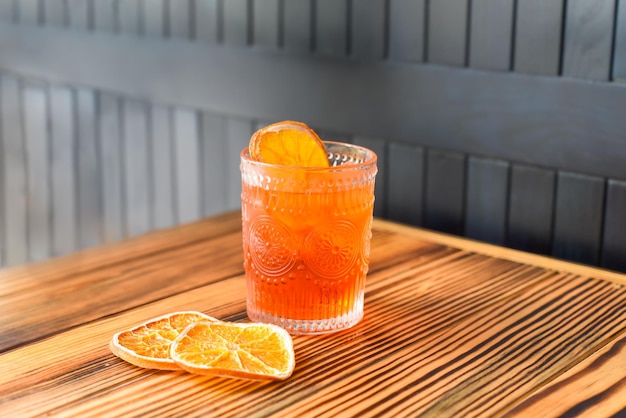 Cocktail de álcool Aperol Spritz com fatia de laranja na mesa de madeira contra a parede escura com espaço de cópia