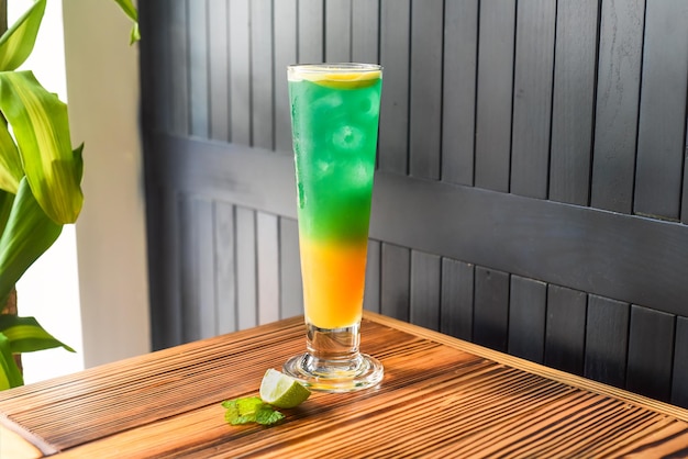 Cocktail de álcool verde amarelo arco-íris na mesa de madeira contra a parede escura com espaço de cópia