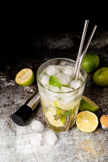 Cocktail de caipirinha de verão fresco em fundo de concreto com limão de frutas verdes na mesa