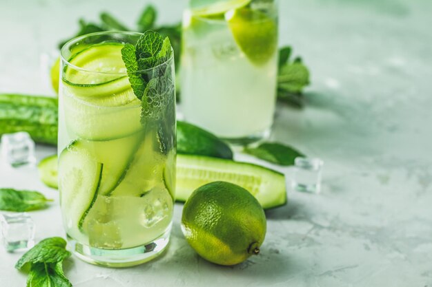 Cocktail de desintoxicação de pepino de menta e coquetel de limão e mojito com limão e hortelã em copos altos em um fundo de superfície de pedra de concreto cinza com espaço de cópia para o seu texto