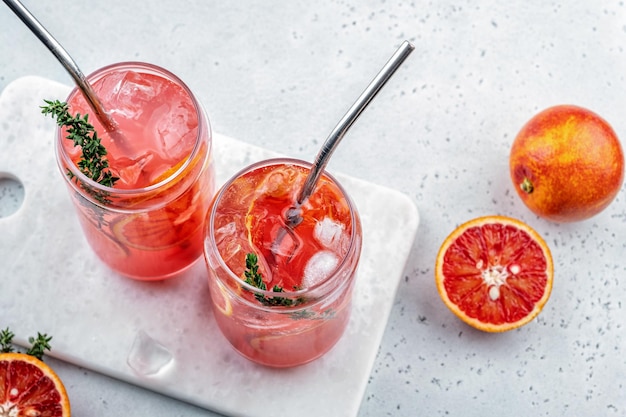 Cocktail de limonada de laranja sanguínea com gelo e tomilho em fundo de concreto cinza claro