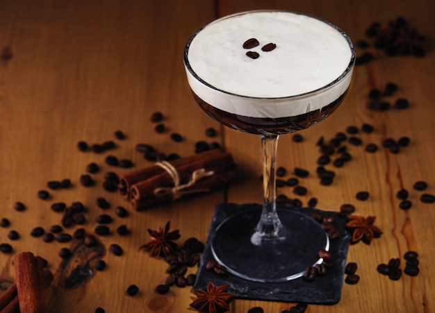Cocktail de martini expresso em um copo com grãos de café, canela e anis estrelado em uma mesa de madeira