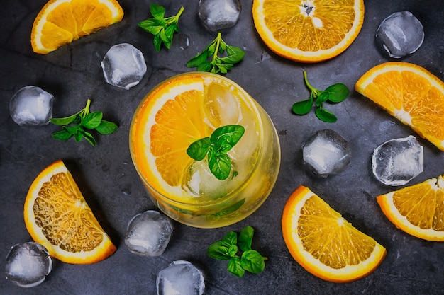 Cocktail frio laranja em vidro transparente em fundo escuro.