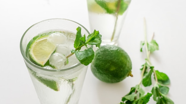 Cocktail gin tonic ou mojito em copo com hortelã, gelo, limão no fundo branco.