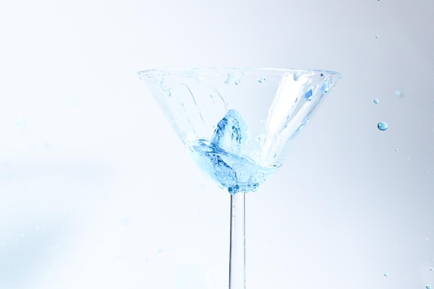 Cocktail mit blauer Flüssigkeit im Glas. Glas mit blauem Wasser, das mit Flüssigkeit mit Spritzern und Tropfen gießt. Martini-Glasfüllung mit Alkohol mit Spritzern auf weißem Hintergrund. Erfrischendes Getränkekonzept.