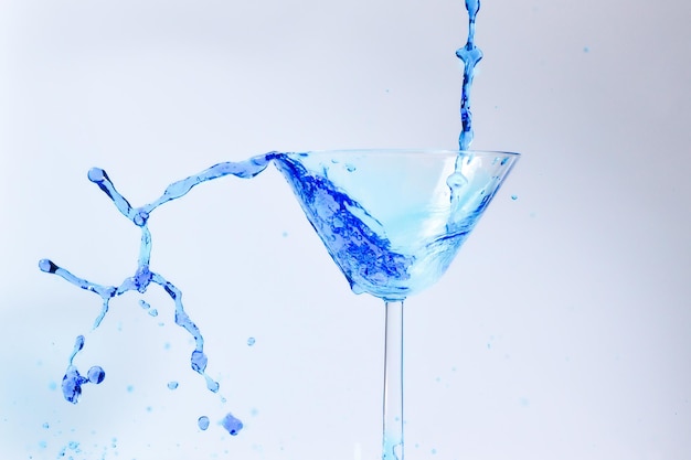 Cocktail mit blauer Flüssigkeit im Glas Glas mit blauem Wasser Gießen mit Flüssigkeit mit Spritzern und Tropfen Martini-Glas-Füllung mit Alkohol mit Spritzern auf weißem Hintergrund Erfrischungsgetränk-Konzept