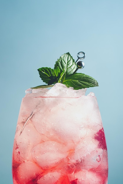 Cocktail não alcoólico com framboesa, provocando cubos de gelo de água mineral, folhas de hortelã decoradas em fundo azul