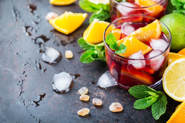 Cocktail tradicional de sangria espanhola fria com vinho tinto e ingredientes em uma mesa preta frutas cítricas laranja limão folhas de hortelã e gelo para os dias quentes de verão Copie o fundo do espaço
