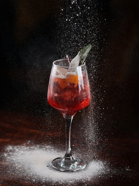 Cocktail vermelho com gelo e cereja em um copo transparente. açúcar de confeiteiro granulado em um cocktail