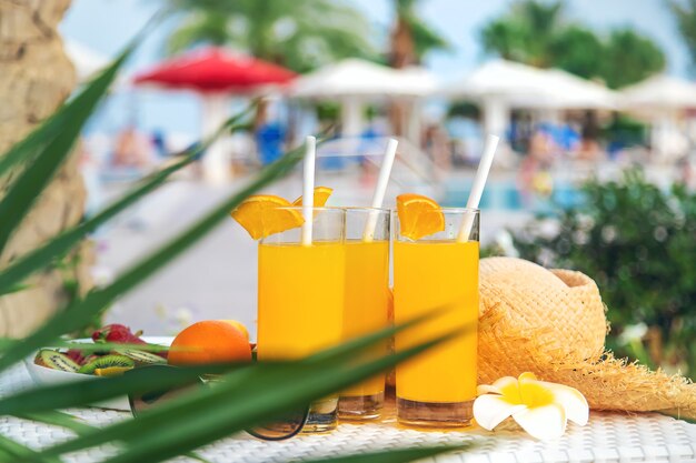 Cocktails, Sonnenbrille, Strohhut und frisches Obst in einer weißen Schüssel am Pool