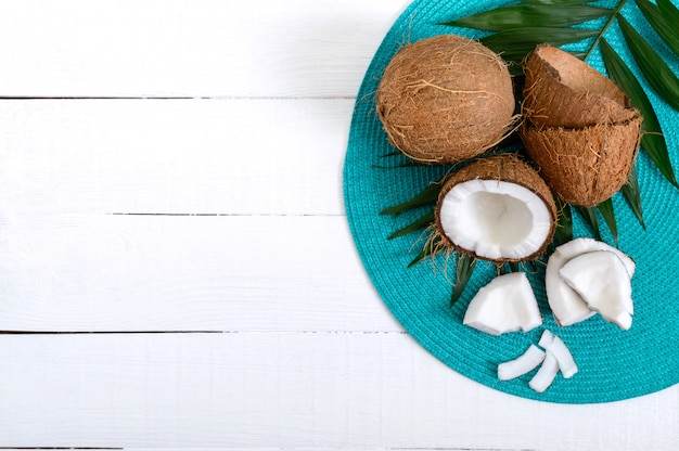 Foto coco. coco entero, cáscara y hojas verdes sobre una mesa de madera blanca. nuez grande frutas tropicales de coco en la cáscara. spa. foto de comida. foto de fondo.