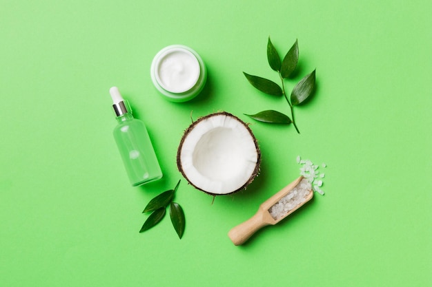 Coco com frascos de óleo de coco e creme cosmético em fundo colorido vista superior espaço livre para o seu texto cosméticos naturais de coco de spa e conceito de tratamento orgânico composição de spa de coco