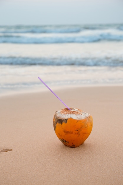 Coco com um canudo na areia à beira-mar