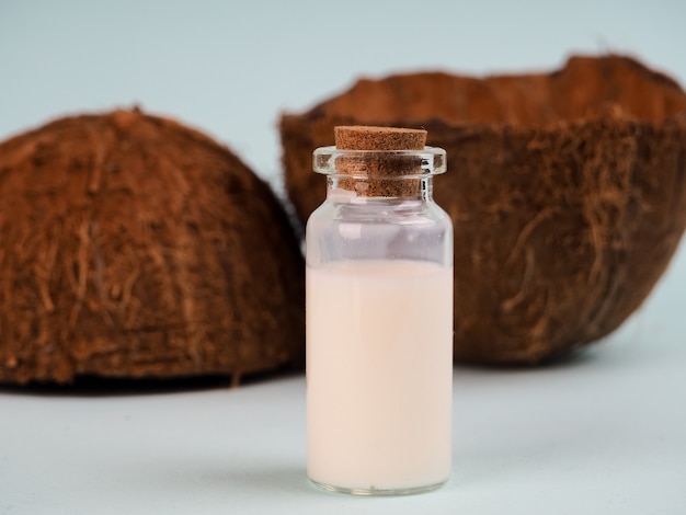 Coco y leche de coco en la mesa azul. Aceite de coco con nuez fresca. leche de coco, aceite de virutas en tubo de ensayo para investigación, superalimento, aceite natural, cosméticos