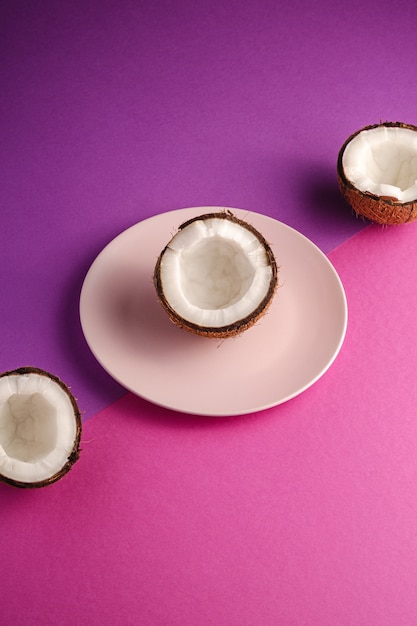 Coco metade na placa-de-rosa com frutos de noz na superfície plana violeta e roxa, conceito tropical comida abstrata, vista de ângulo